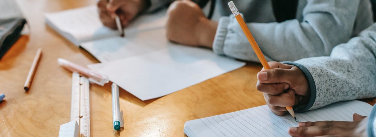 crop pupils writing in copybook on desk